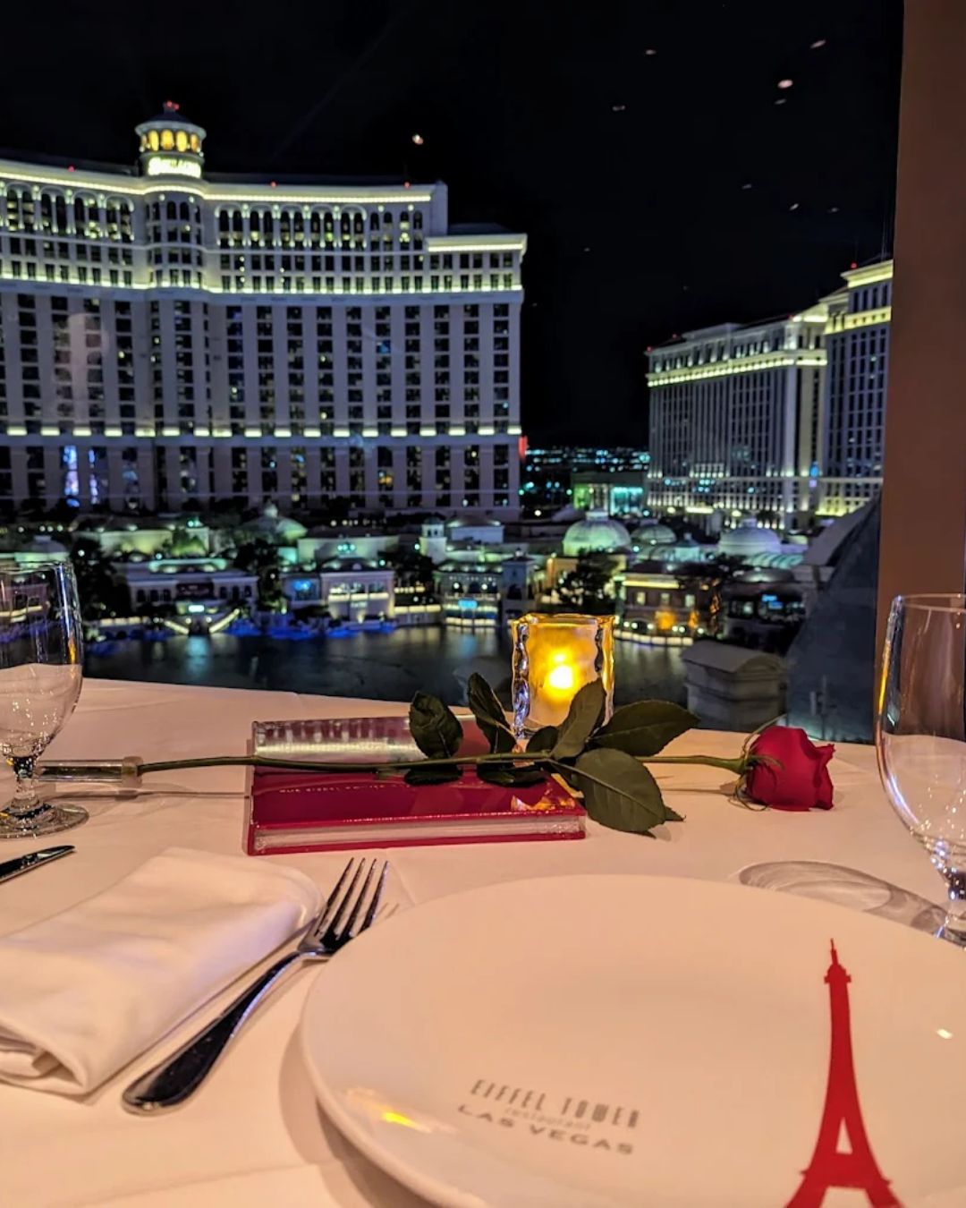 View from an internal table at Eiffel Tower Restaurant, Paris Las Vegas. Golden Crème Brûlée French Toast sits in the foreground, and the Bellagio fountains are exploding with water outside the window in daylight.