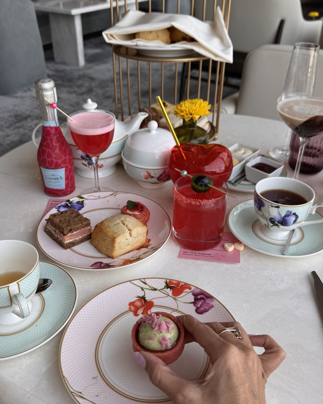 A tiered tray of delicate tea sandwiches and scones sits on a table at Peacock Alley, with floor-to-ceiling windows showing the Las Vegas skyline.