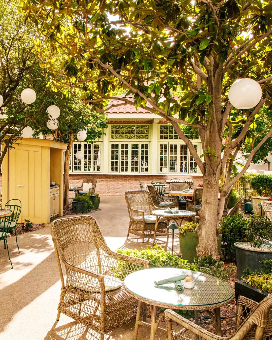 A chic, sunlit garden patio scene at Primrose, Park MGM, evoking a South of France vibe. A table is set with soft daylight, sparkling rosé, a striped umbrella, and a Croque Madame.