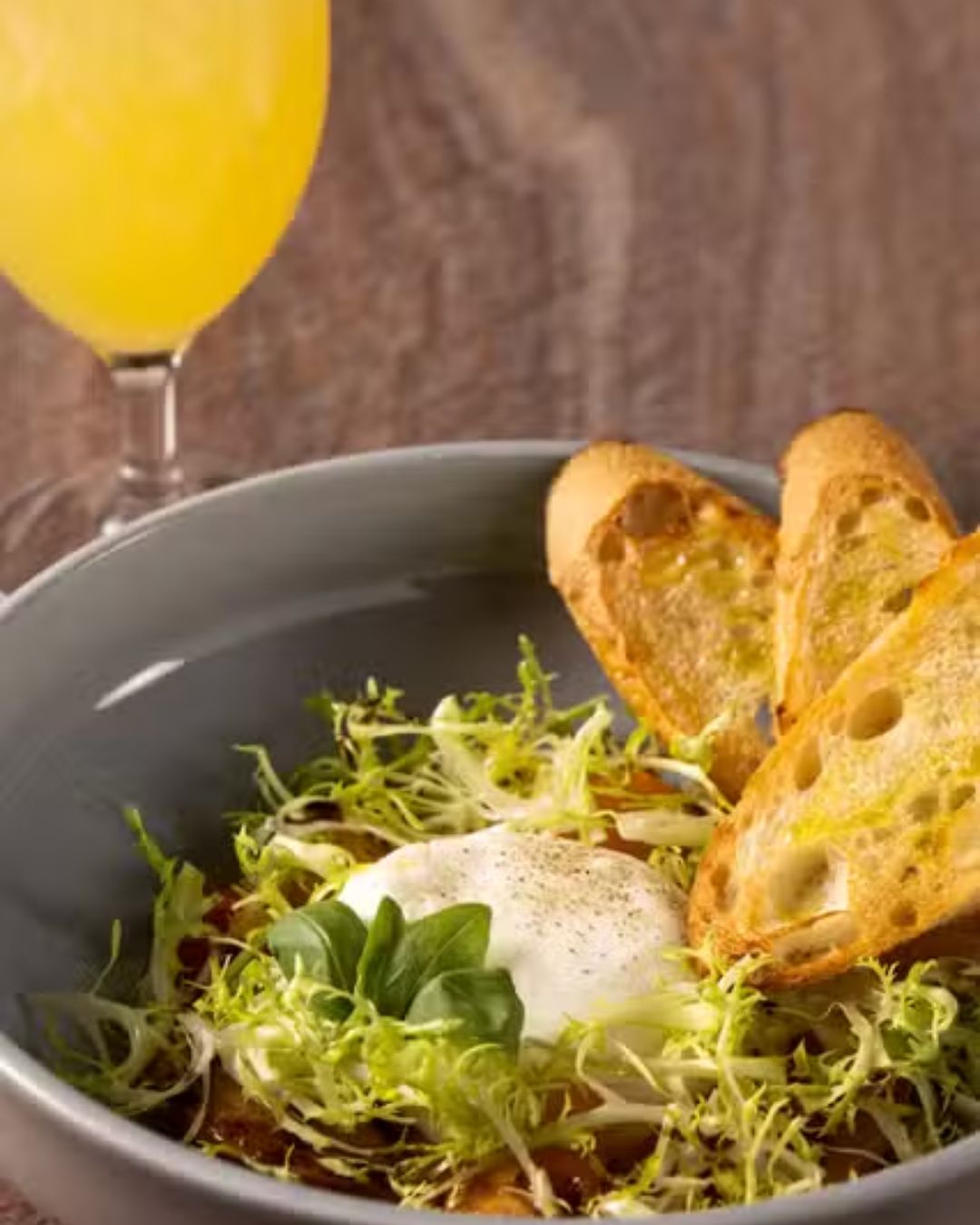 A serene morning view of the lush, palm-lined outdoor terrace at Veranda, Four Seasons Las Vegas. An elegant table setting holds a plate of Lemon Ricotta Pancakes garnished with berries.