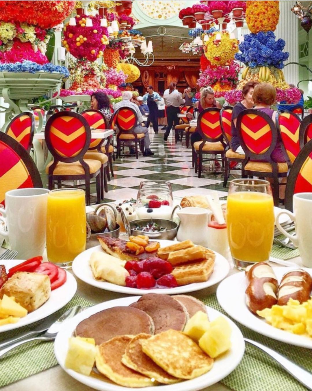 A vertical view of the maximalist floral decor inside The Buffet at Wynn Las Vegas. Below a canopy of roses and hydrangeas, a lavish display of fresh pastries and chilled seafood is set for brunch.